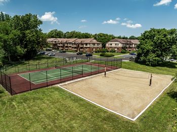 A tennis court surrounded by a fence and trees with apartment buildings in the background